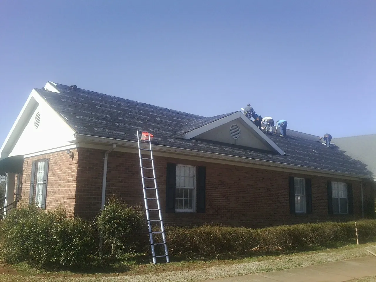 Crew tearing shingles off a brick ranch roof with a ladder set — Metal Roof Repair work by our crew in Pope Army Airfield