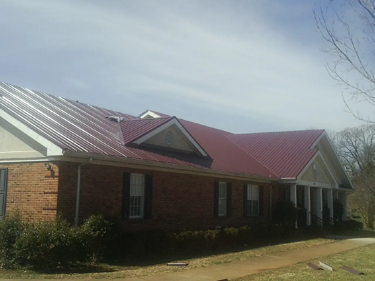 Red metal roof with gabled entries on a long brick building, from a Hail Damage Roof Repair job in Pope Army Airfield