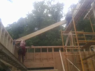 Carpenter raising a rafter beam on a new second story frame in Pope Army Airfield