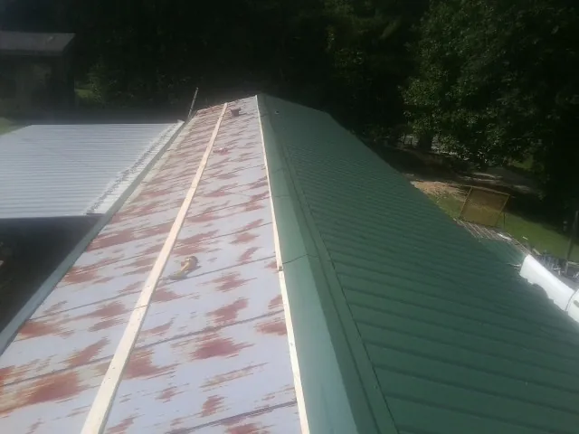 Old rusted panels beside newly installed green metal roofing — Wind Damage Roof Repair by Roofing Brothers in Pope Army Airfield