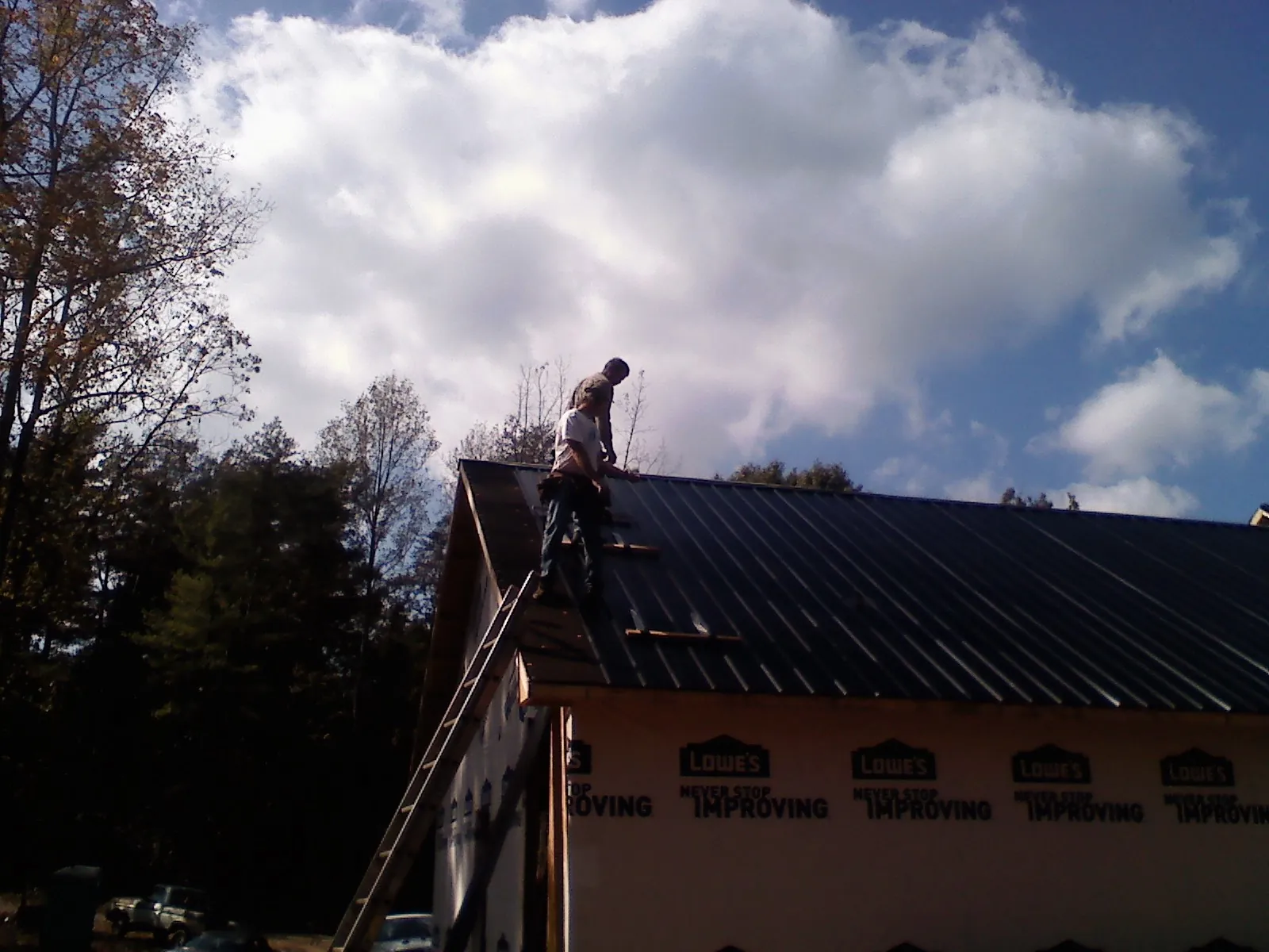 Roofer fastening dark metal panels high against a cloudy sky, from a Roof Inspection job in Pope Army Airfield