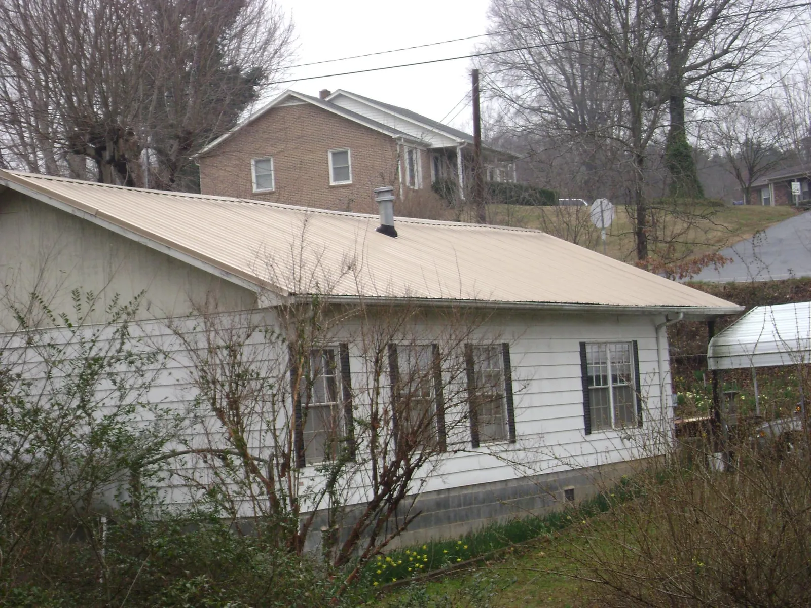 Tan metal roof on a white sided house set into a hillside — Commercial Roofing by Roofing Brothers in Pope Army Airfield