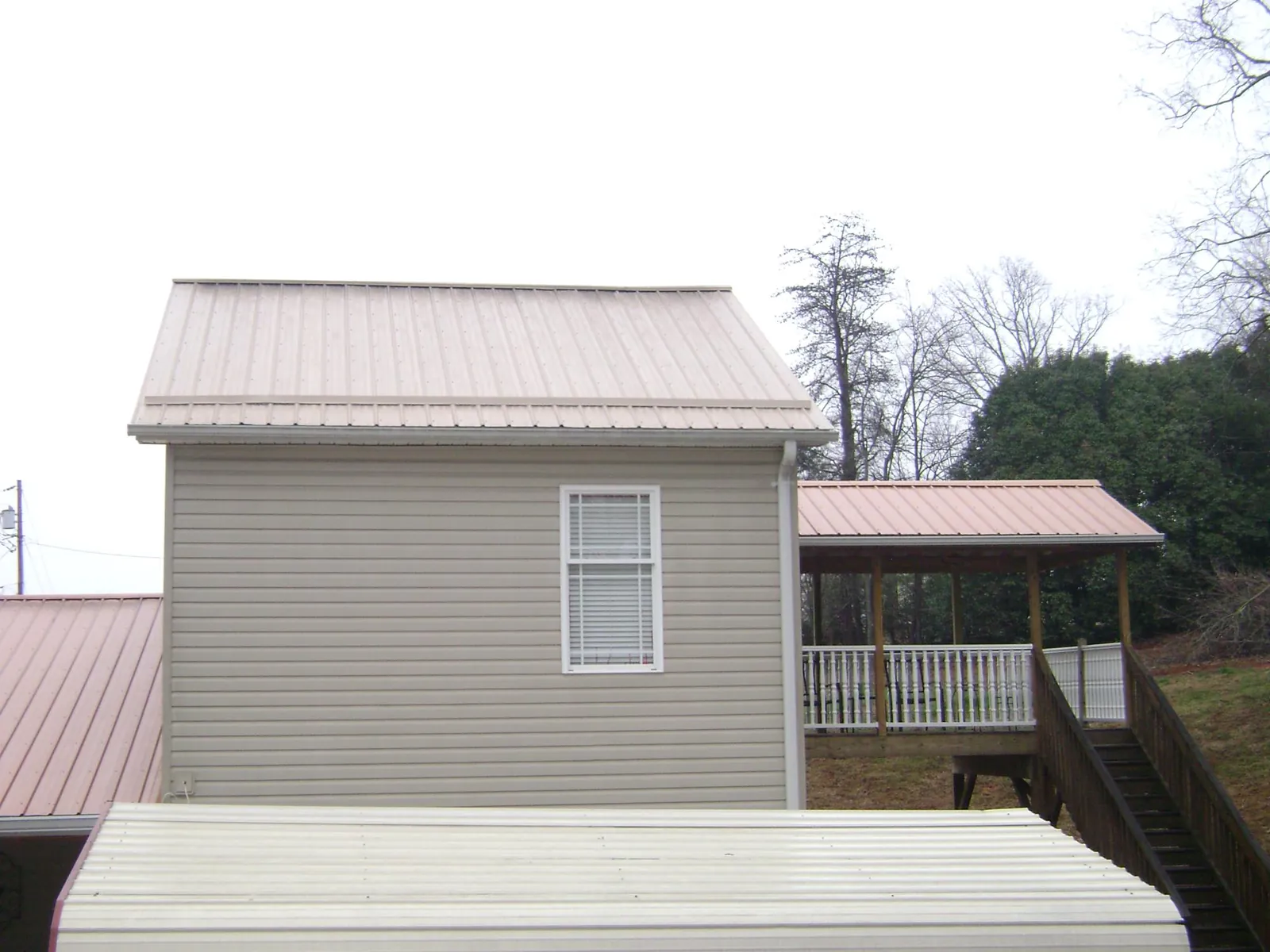 Tan metal roofs on a two story addition and attached porch, from a Roof Replacement job in Pope Army Airfield